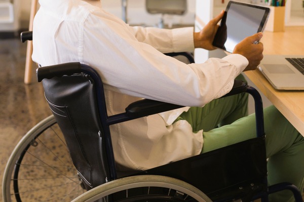 Persona en silla de ruedas con tablet en oficina, simboliza una incapacidad total cualificada con posibilidad de trabajar en otro sector.