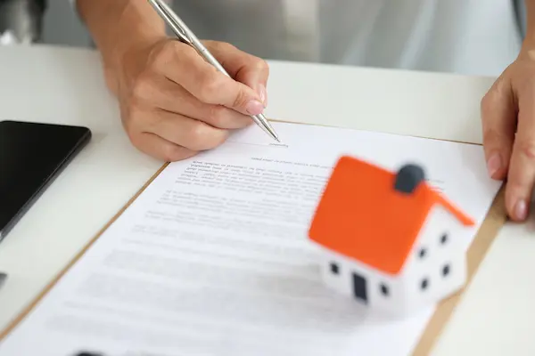 Persona firma contrato junto a maqueta de casa, ilustrando la validez de arras firmadas por inmobiliaria en compraventa.
