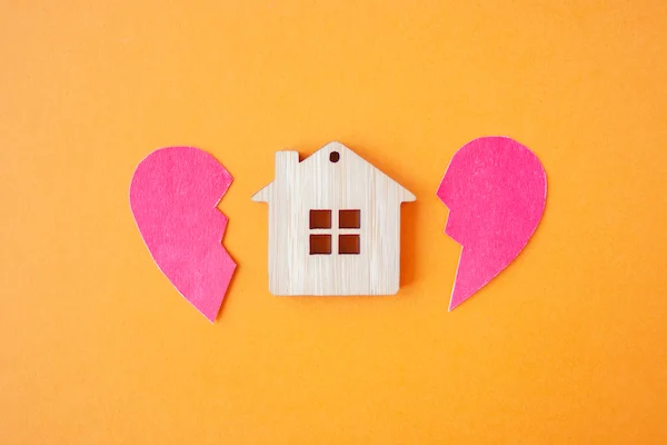 Casa de madera entre corazón roto, representa el reparto de la vivienda común tras un divorcio.