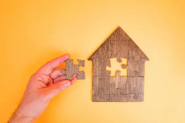 Mano sosteniendo pieza de puzzle para completar una casa, representando la extinción de condominio.