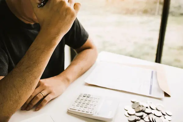 Hombre calculando el impuesto de sucesiones en Madrid con monedas, factura y calculadora sobre la mesa.