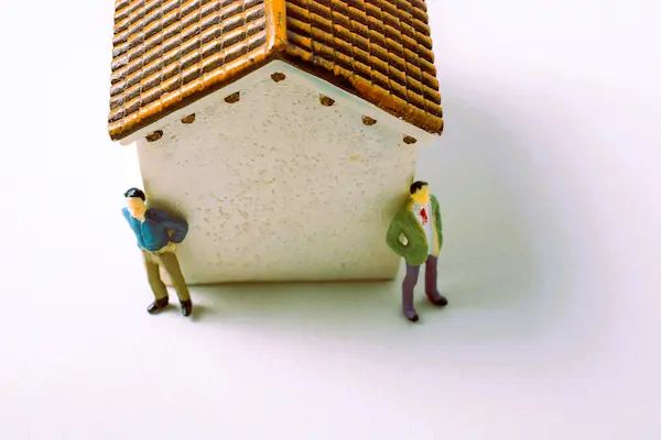 Dos figuras junto a una casa simbolizan cómo se reparte una herencia de una vivienda entre hermanos.