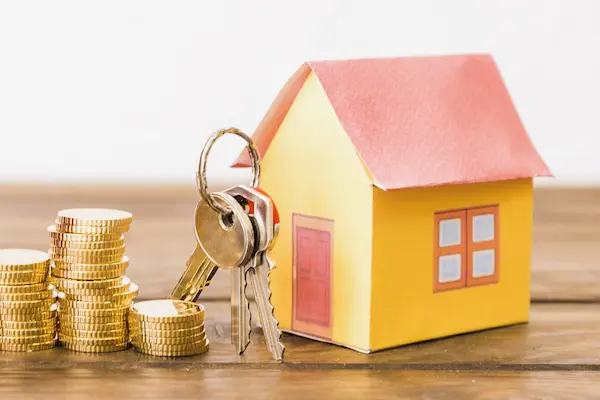 Casa en miniatura con llaves y monedas simboliza cómo repartir una herencia a partes iguales entre herederos.