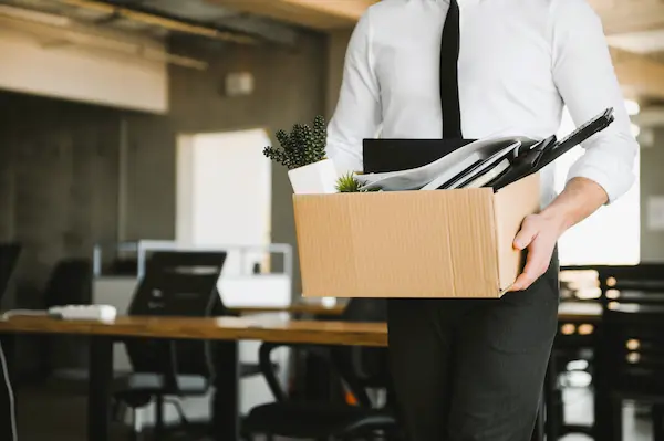 Empleado con caja de pertenencias dejando la oficina, simbolizando el despido de personal de alta dirección.
