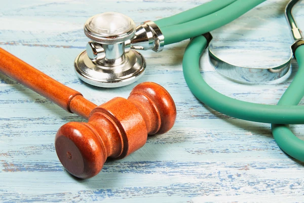 Mazo judicial junto a un estetoscopio sobre mesa azul, simbolizando la aplicación legal de la Lex Artis médica.