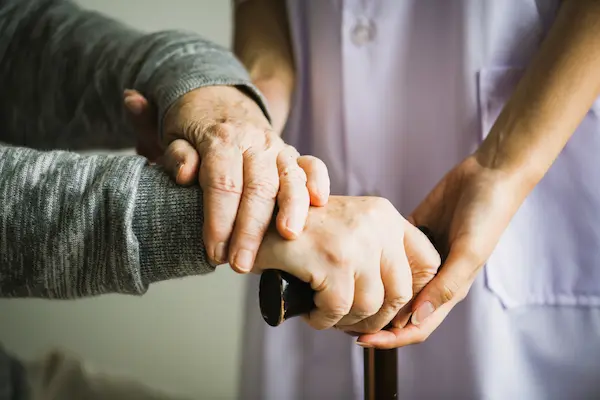 Manos de anciano apoyadas en un bastón, sujetadas por una cuidadora, en referencia a negligencias en residencias.