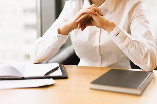 Mujer con camisa blanca en oficina, manos entrelazadas sobre la mesa, representa la preparación para un recurso de alzada.