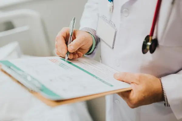 Médico rellenando un formulario clínico, relacionado con el proceso de reclamación por retraso en cribados de cáncer de mama en Andalucía.
