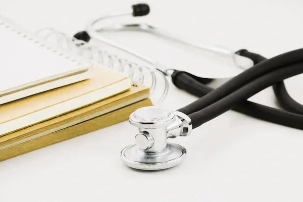 Estetoscopio y cuadernos sobre mesa blanca, representando la denuncia de una negligencia médica en la Seguridad Social.
