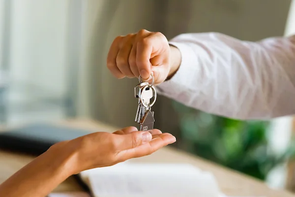 Persona entregando llaves de una vivienda, ilustrando el derecho de tanteo y retracto en transmisiones inmobiliarias.