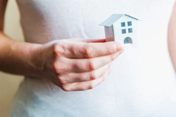 Persona sostiene una maqueta de casa blanca, simbolizando la descalificación de una Vivienda de Protección Oficial (VPO).