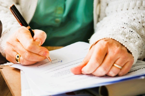 Manos de persona mayor firmando documentos legales, en el contexto de la impugnación de un testamento.