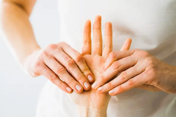 Manos examinando una palma dolorida, símbolo de las poliartralgias que pueden derivar en incapacidad laboral.
