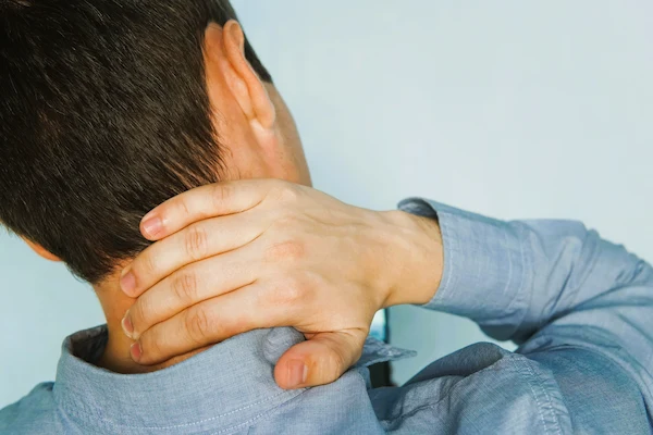 Hombre con camisa sujetándose el cuello tras un posible latigazo cervical, lesión común en accidentes de tráfico.