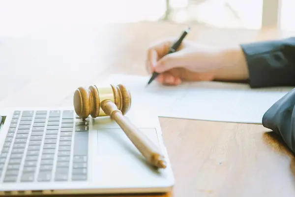 Mazo judicial sobre portátil junto a mano redactando, en contexto de reformas legales contencioso-administrativas.