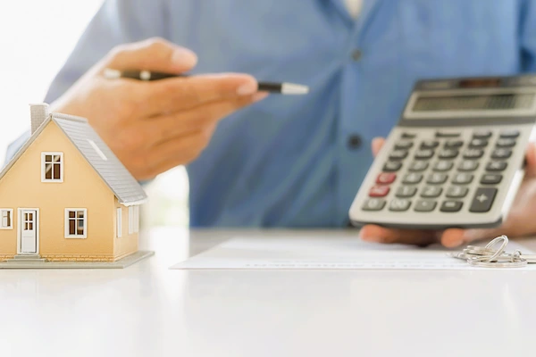Persona con calculadora y maqueta de casa, analizando los impuestos asociados a la venta de una vivienda en España.