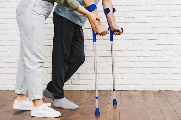 Persona con muletas recibe ayuda para caminar, en relación con revisión de la incapacidad permanente total.