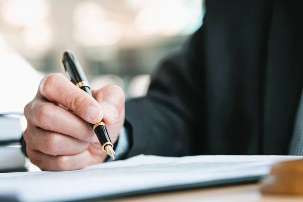 Mano masculina firmando documentos legales, aludiendo a la posibilidad de impugnar un testamento notarial.