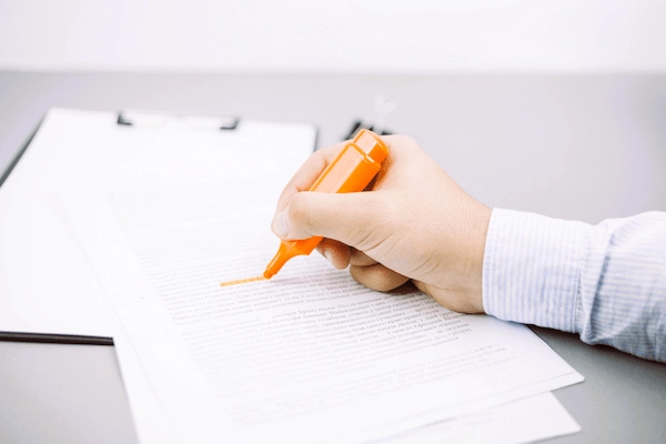 Mano subrayando documento legal, representando el análisis de un posible delito de falsedad documental.