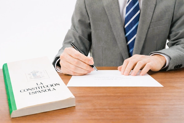 Persona redacta un documento junto a un ejemplar de la Constitución Española, en el contexto de recursos de amparo.