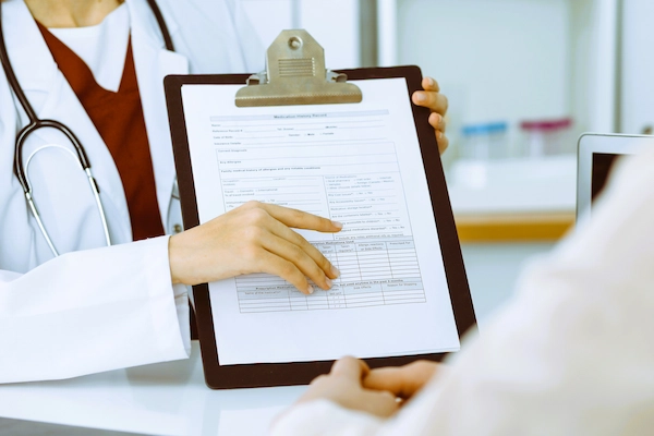 Médico muestra historial clínico a paciente, ilustrando la evaluación para una posible indemnización por negligencia médica.