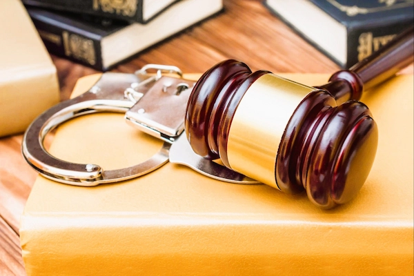 Mazo judicial y esposas sobre un libro legal, simbolizando el delito de estafa procesal en procedimientos judiciales.