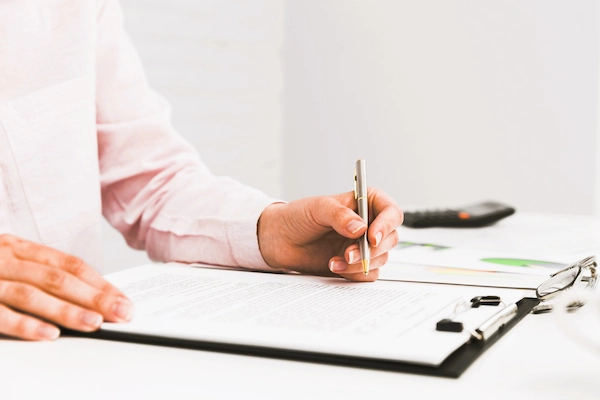 Persona firma documento mercantil con bolígrafo, representando el delito de falsificación documental.