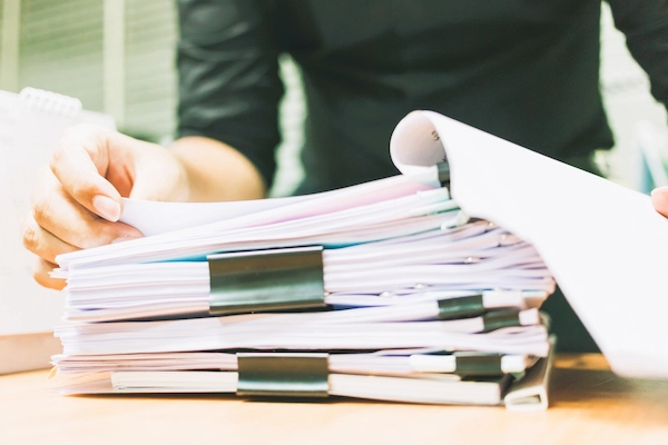 Manos revisando expedientes que representan documentación en casos de fraude a la Seguridad Social.