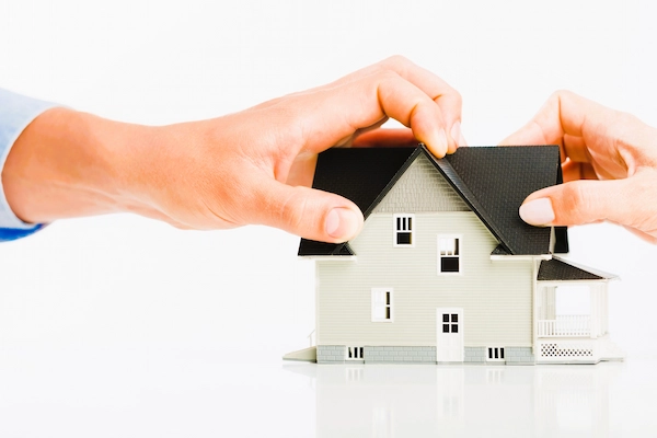 Manos sostienen maqueta de casa, simbolizando el usufructo y su posible extinción sobre una vivienda en contexto legal.