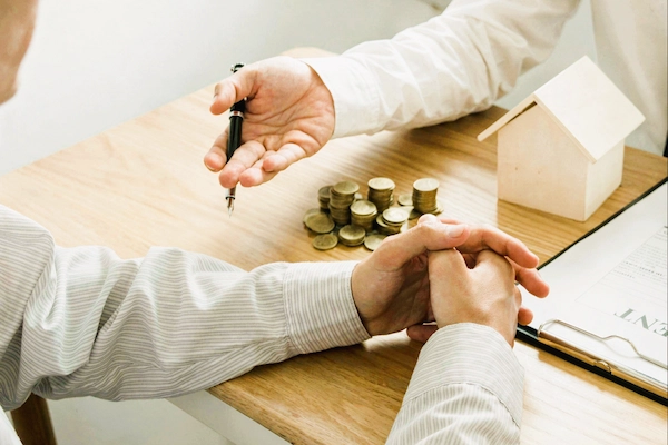 Negociación sobre el tercio de libre disposición con monedas, contrato y maqueta de casa sobre la mesa.