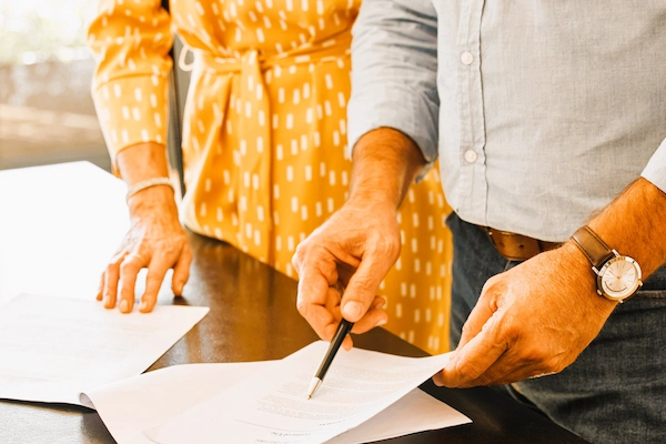 Dos personas revisan y firman documentos legales, ilustrando el proceso de realizar un testamento abierto.