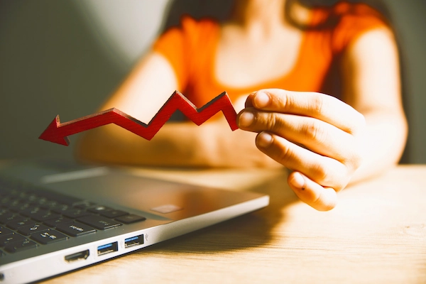Trabajadora frente a portátil sostiene flecha roja descendente, símbolo de bajo rendimiento laboral en la empresa.