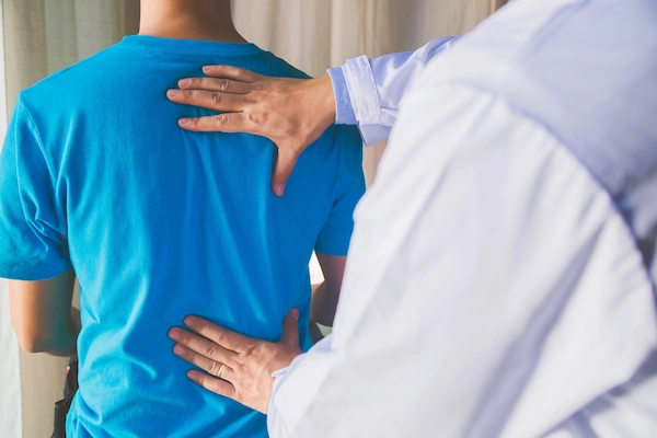 Médico explorando la espalda de un paciente, posible caso de pérdida de oportunidad médica por diagnóstico tardío.