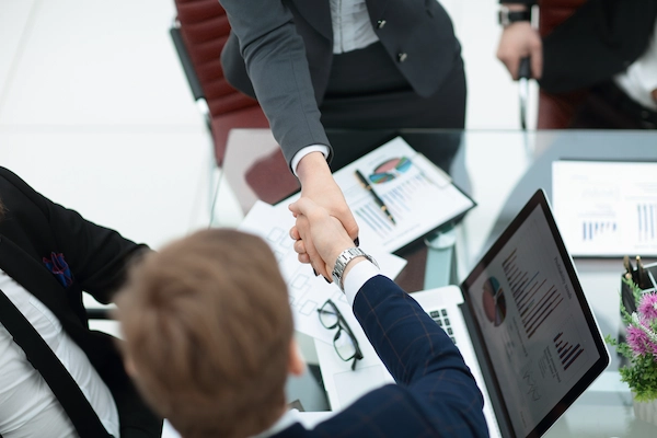 Apretón de manos entre empresarios en oficina sobre la venta de empresa y continuidad de trabajadores.