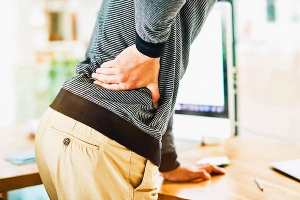 Trabajador con dolor lumbar apoyado en un escritorio, representando la incapacidad laboral por síndrome facetario lumbar.