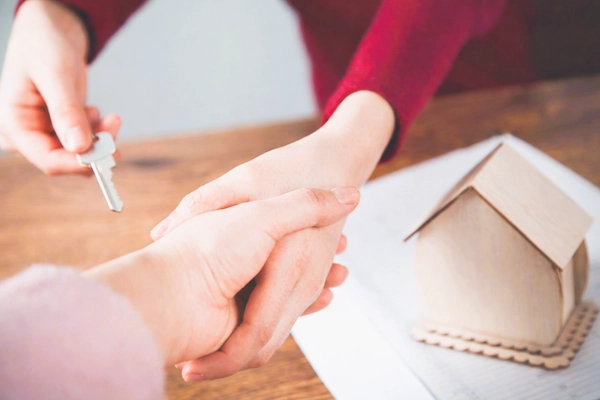 Entrega simbólica de una llave de vivienda entre dos personas junto a una maqueta de casa, ilustrando el usufructo del 50 % de una vivienda: derecho a usar y disfrutar la propiedad sin ser el propietario total.