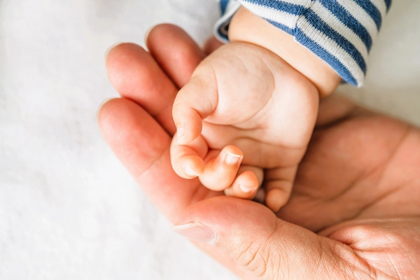 Mano de recién nacido agarrando dedo adulto, representando la distocia de hombros, complicación del parto donde el hombro queda atrapado.
