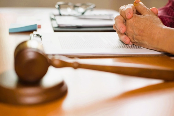 Persona con manos entrelazadas ante documentos y mazo judicial, representando solicitud de ejecución de sentencia judicial