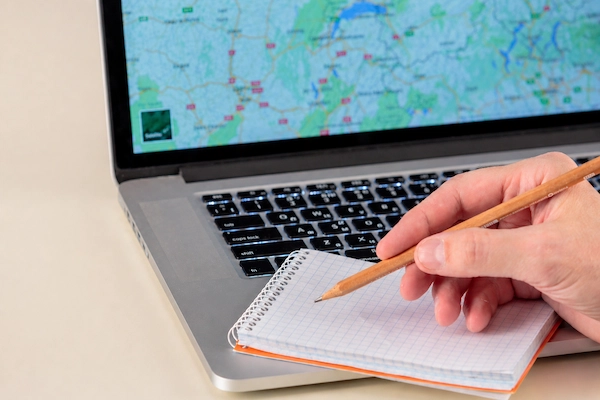 Mano tomando notas junto a portátil y dinero; representa movilidad geográfica laboral, traslado por trabajo a otra ubicación