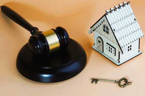 Mazo judicial junto a una casa y una llave, representando la cesión de remate, transmisión del derecho a adquirir un inmueble subastado.