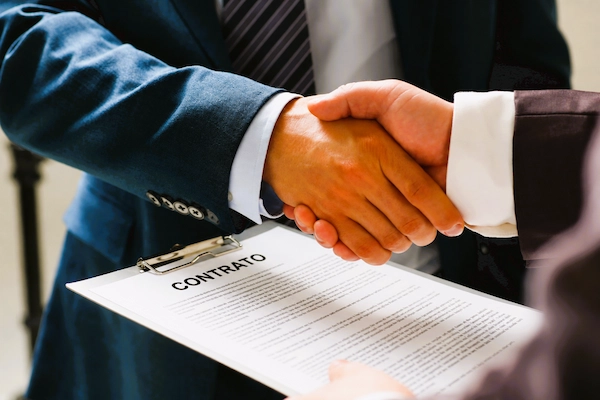Apretón de manos sobre un contrato mercantil, acuerdo comercial que regula derechos y obligaciones entre las partes.