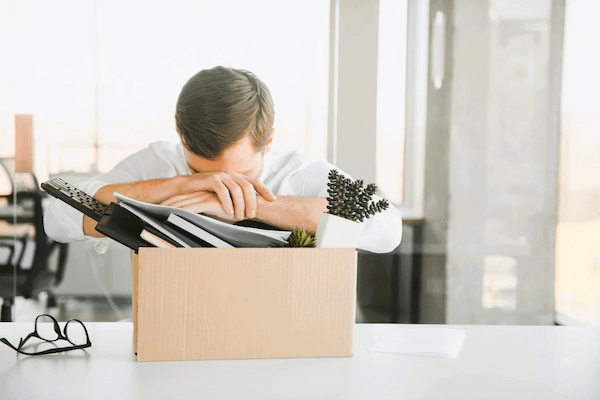 Trabajador afectado por un despido improcedente, apoyado sobre una caja con objetos de oficina tras perder su empleo.