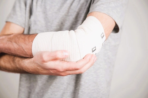 Trabajador con el brazo vendado por accidente laboral, relacionado con la incapacidad permanente total para ejercer su profesión habitual.