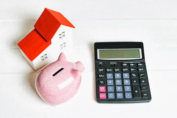 Calculadora, hucha y casa en miniatura, representando el cálculo de la liquidación de gananciales tras un divorcio.