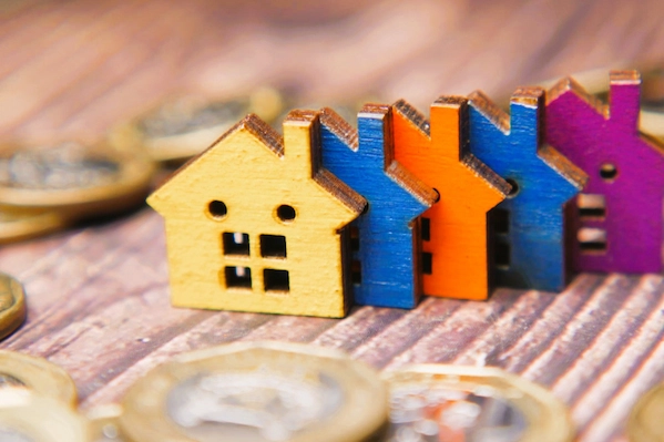 Casas de madera de colores junto a monedas, representando una sociedad patrimonial, empresa creada para gestionar bienes.