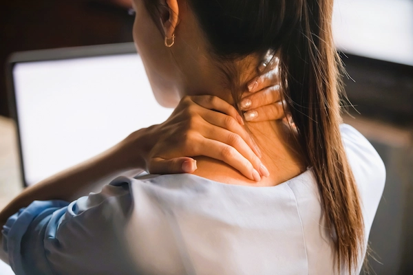 Mujer con dolor de cuello por cervicalgia crónica, afección cervical persistente que puede causar incapacidad laboral.