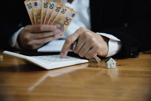 Persona contando billetes y calculando el impuesto de donaciones en Madrid, junto a pequeñas casas que representan el patrimonio.