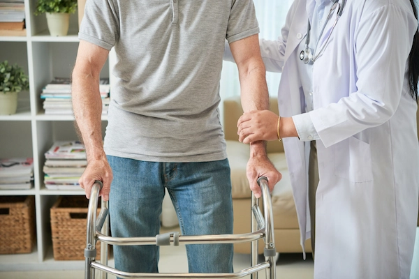 Profesional sanitaria ayuda a caminar a un hombre con andador, ejemplo de incapacidad permanente parcial para trabajar.